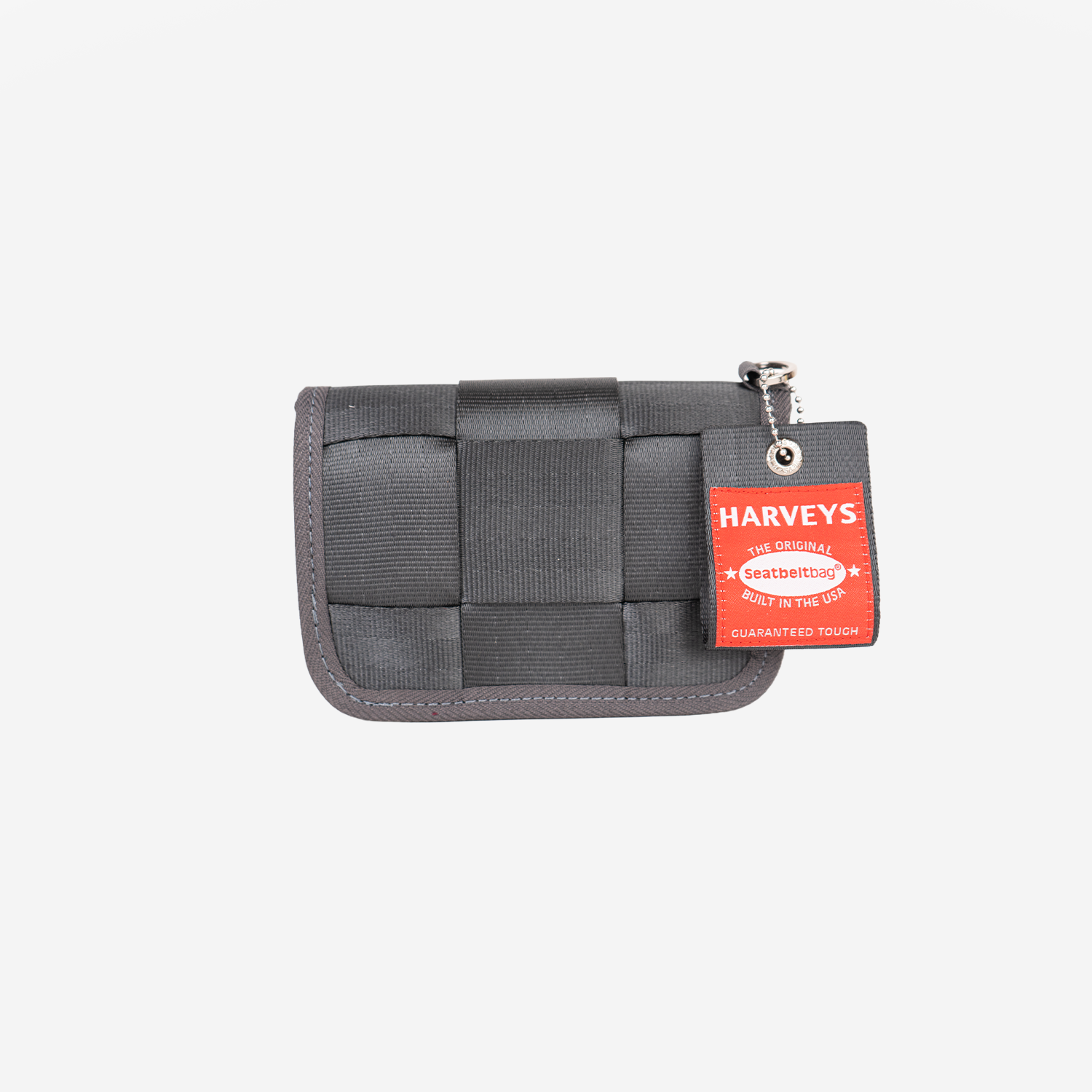 A dark gray woven seatbelt wallet with a black strap closure and a red Harveys Tag attached on the right side, set against a plain light gray background.