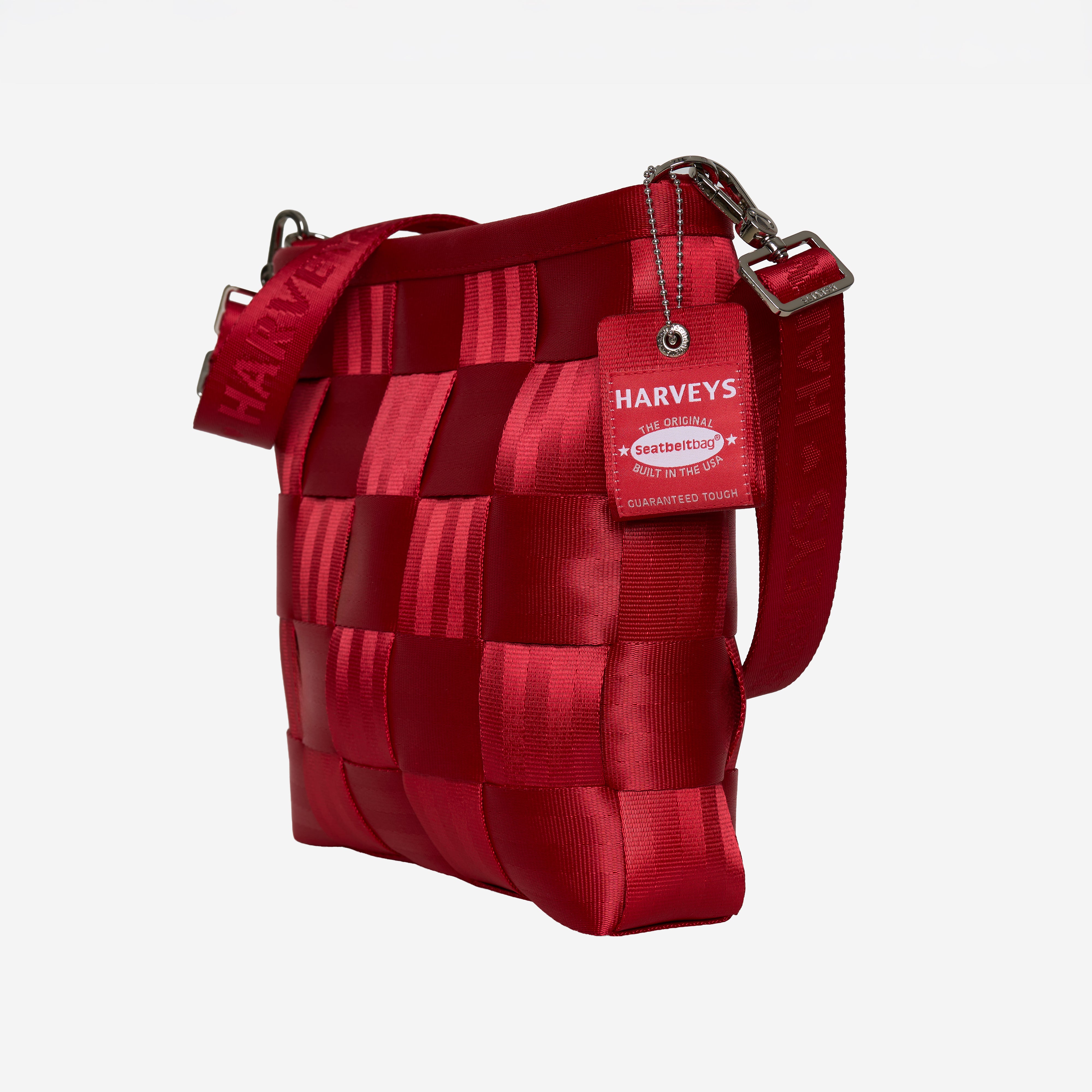 A red woven seatbelt crossbody bag with a matching red strap and a hanging red tag that reads HARVEYS, shown on a plain light gray background.
