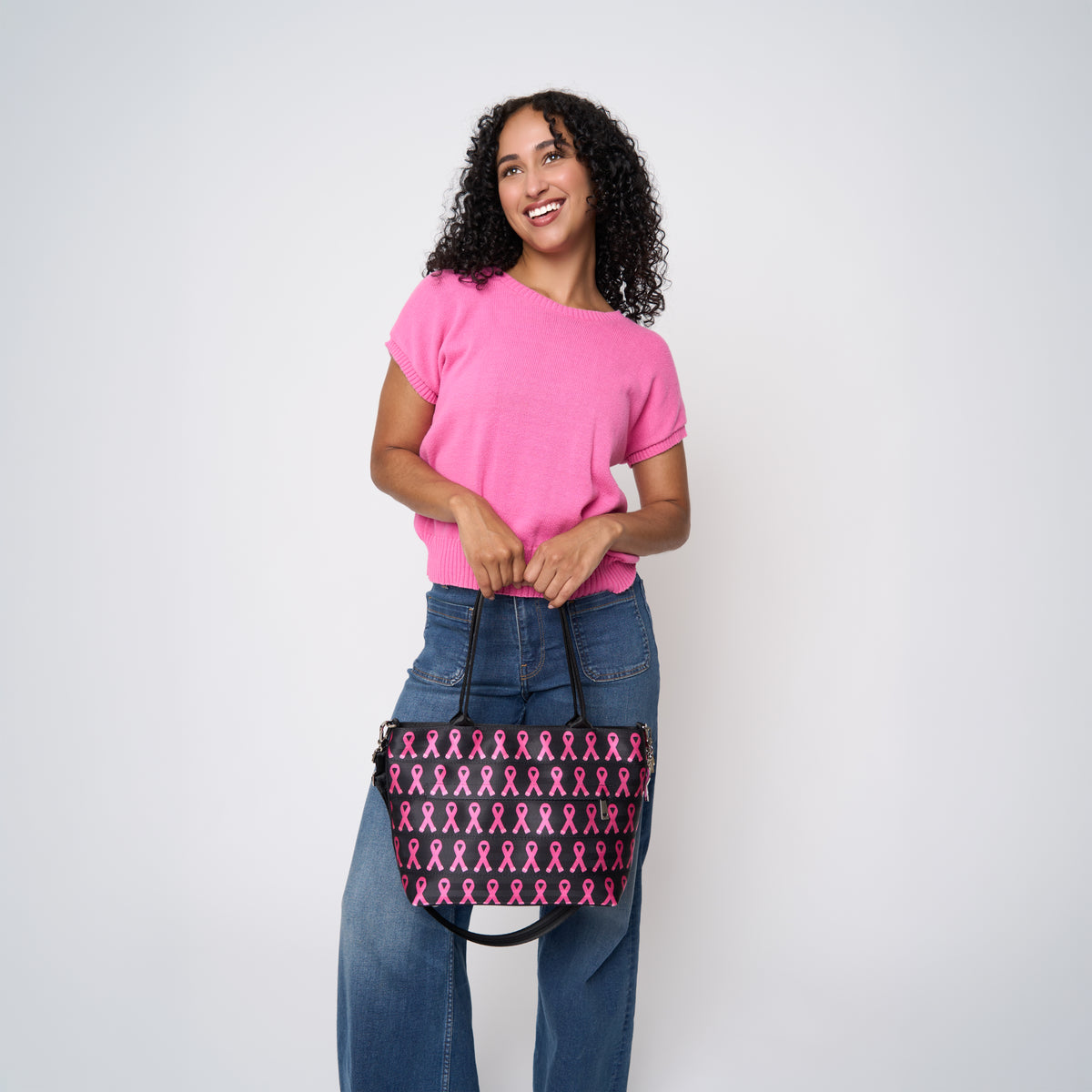 A model wearing The Pink Agenda Pink Ribbon Mini Streamline Tote