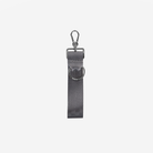 A dark gray seatbelt keychain with a silver metal swivel snap hook and a matching silver metal D-ring, shown against a plain light gray background.