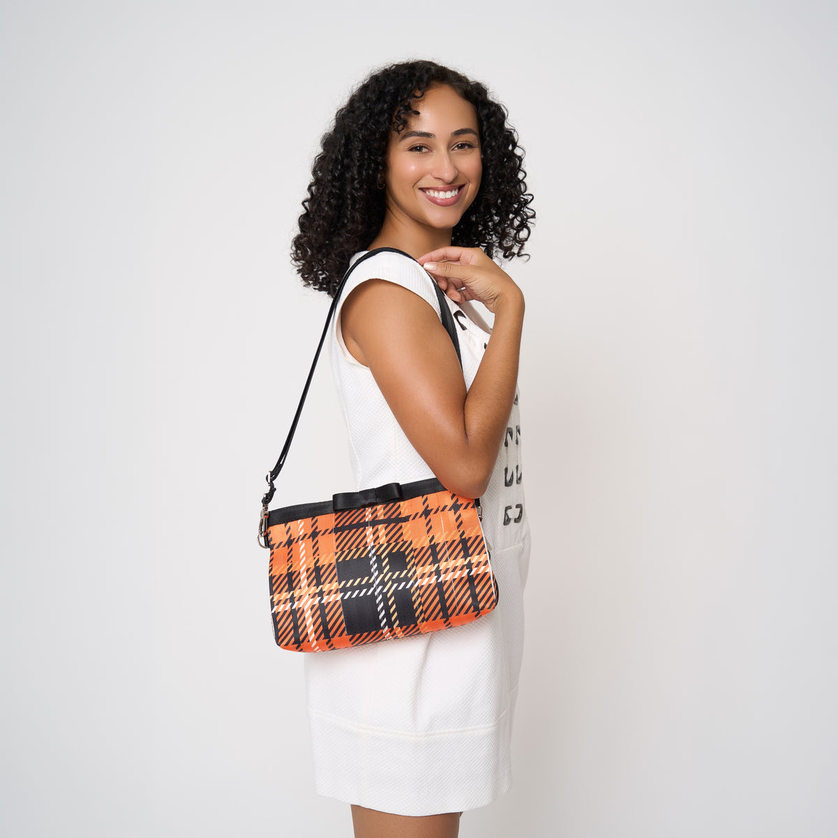 Model carrying Bow Clutch in orange tartan with adjustable black strap