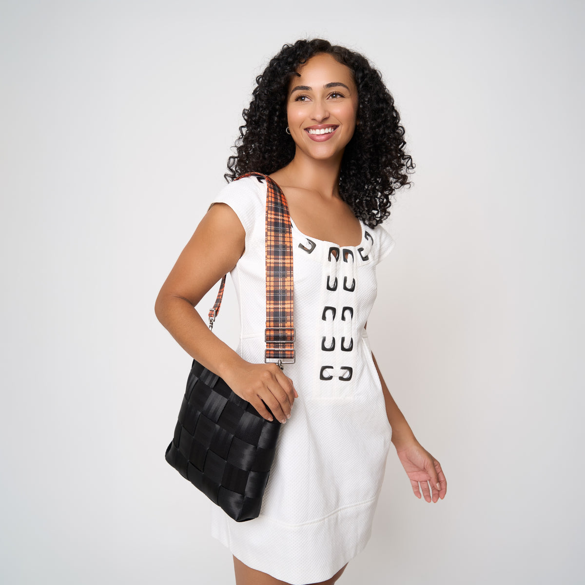 Model carrying 5 panel  Click N Carry in Orange Tartan attached to black mini messenger