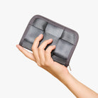 A hand holding a gray zippered wallet  shown against a plain white background.
