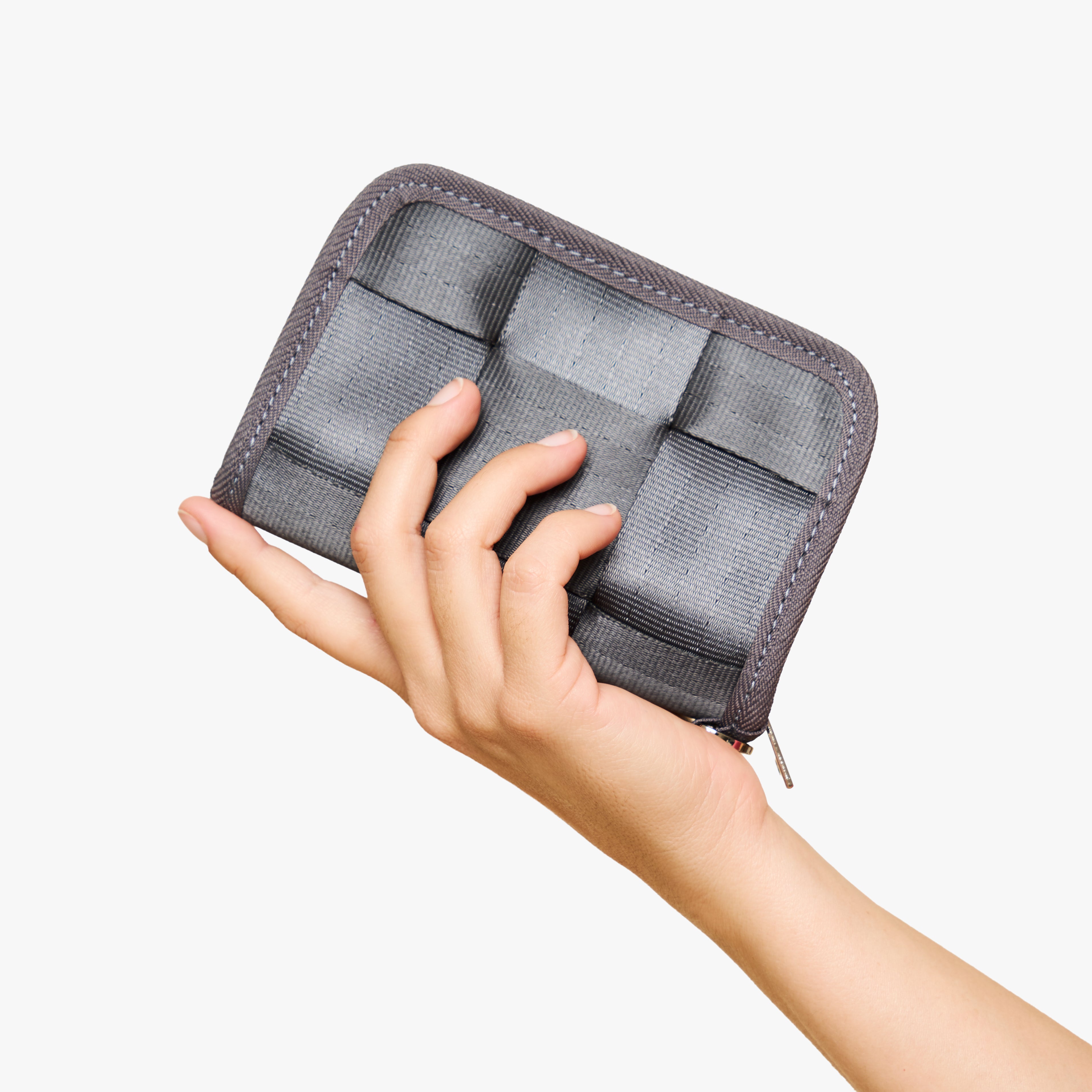 A hand holding a gray zippered wallet  shown against a plain white background.