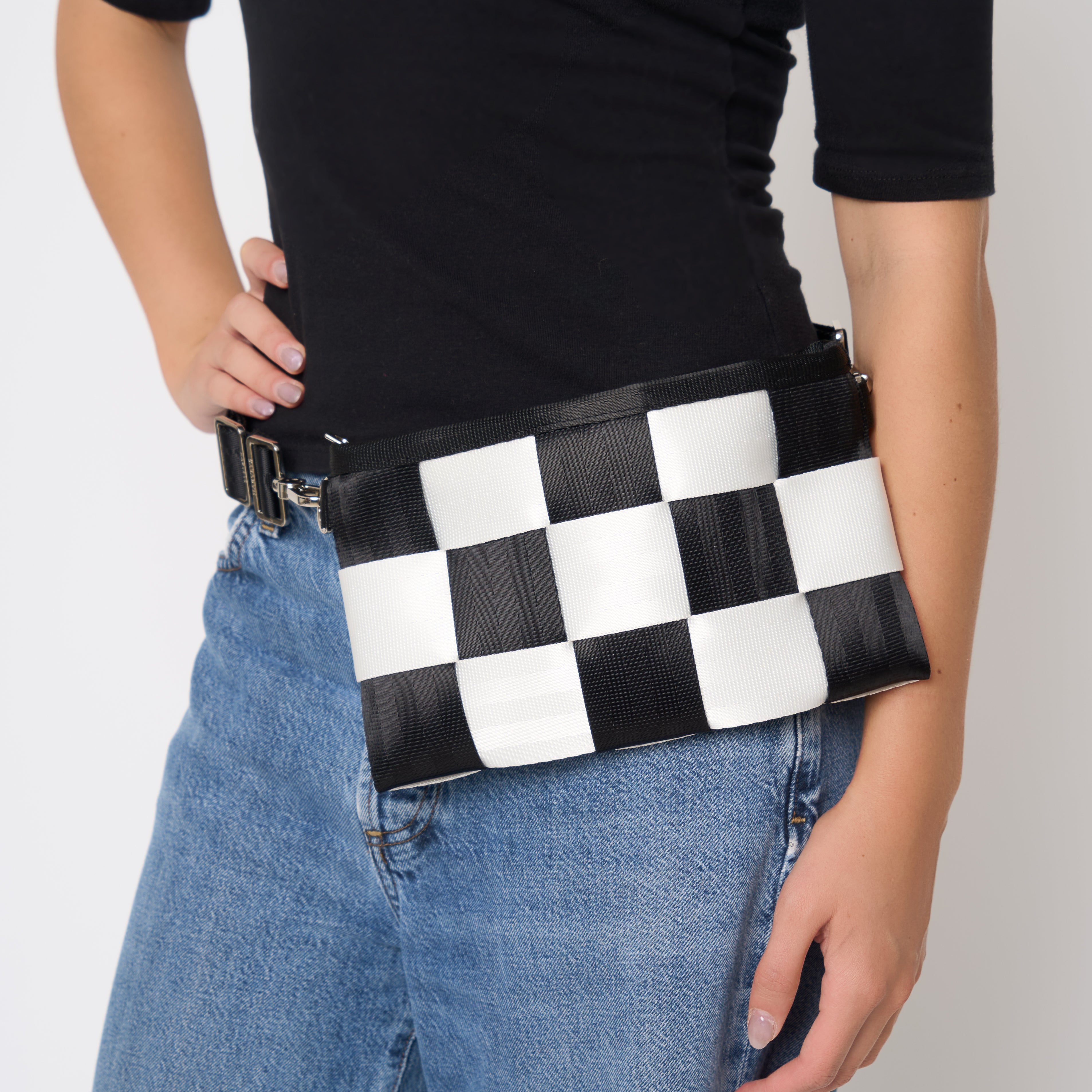 A black and white checkered Hip Pack being worn around the waist bag by a model wearing a black t-shirt and blue jeans.