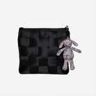 A black woven mini messenger bag with a zipper closure, featuring a small gray plush dog keychain with a colorful pattern attached on a key ring, set against a plain light gray background.