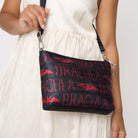 Model wearing black clutch with red Dracula and bat lettering and silver bat charm