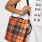 Close up of model carrying Medium Streamline Tote in orange tartan with adjustable black strap