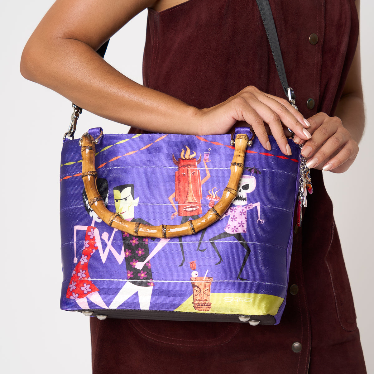 Close up of model using extendable black strap to carry Mini Streamline Tote Shag Tiki Dance Party