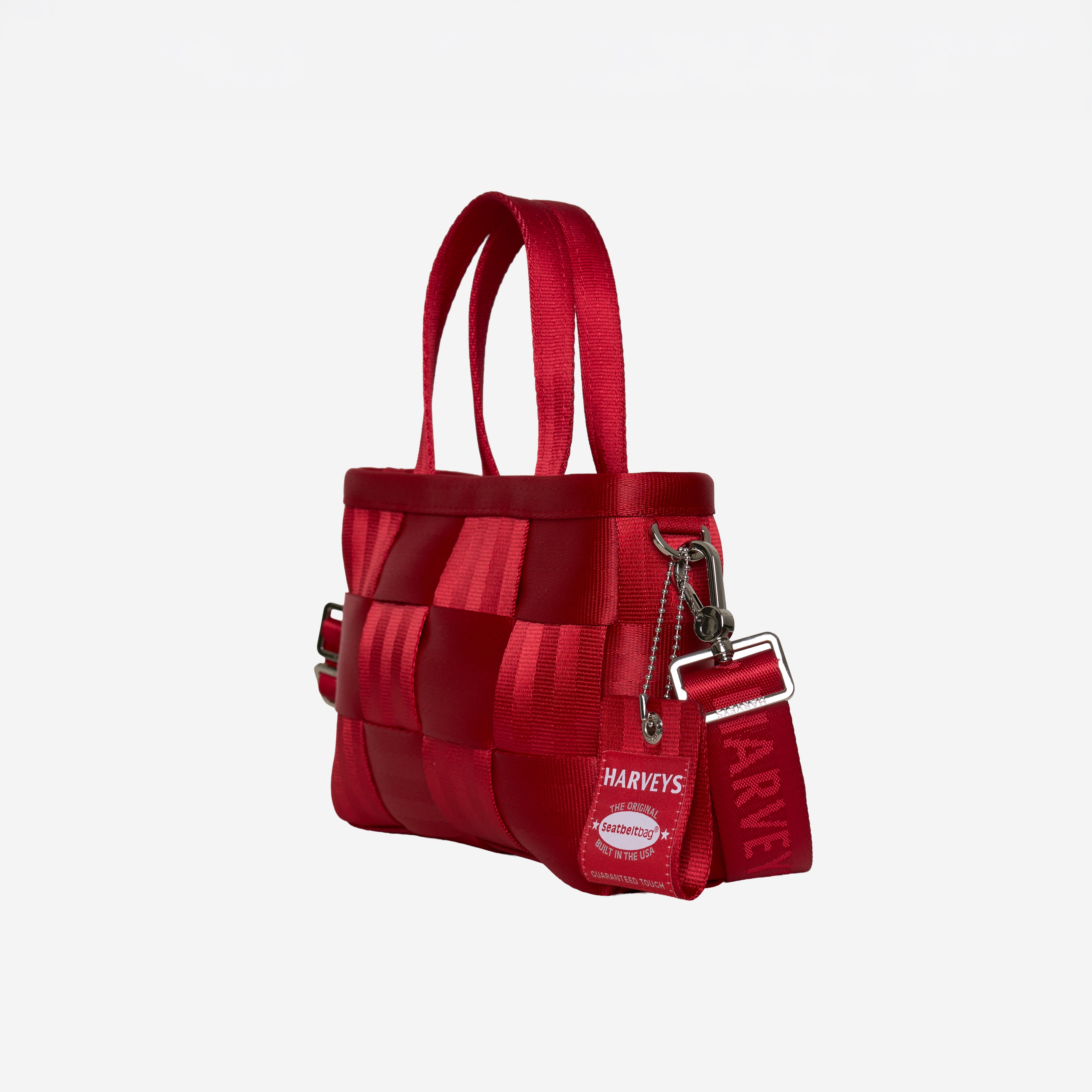 A red woven seatbelt handbag with double top handles, a detachable shoulder strap, and a hanging tag that reads HARVEYS, shown on a plain light gray background.