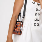 Model holding woven petite tote in orange tartan with adjustable black strap