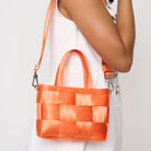 Close up of model using adjustable strap to carry woven petite tote orange