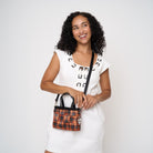 Model holding woven petite tote in orange tartan with adjustable black strap